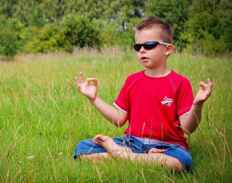 mental health meditation. Young boy in red shirt and sunglasses sits cross lemeditatinggged 