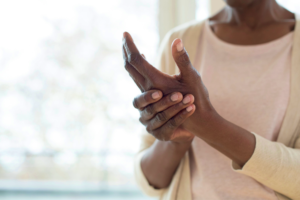 joint pain. African American woman in white shirt rubbing one hand with the other in pain